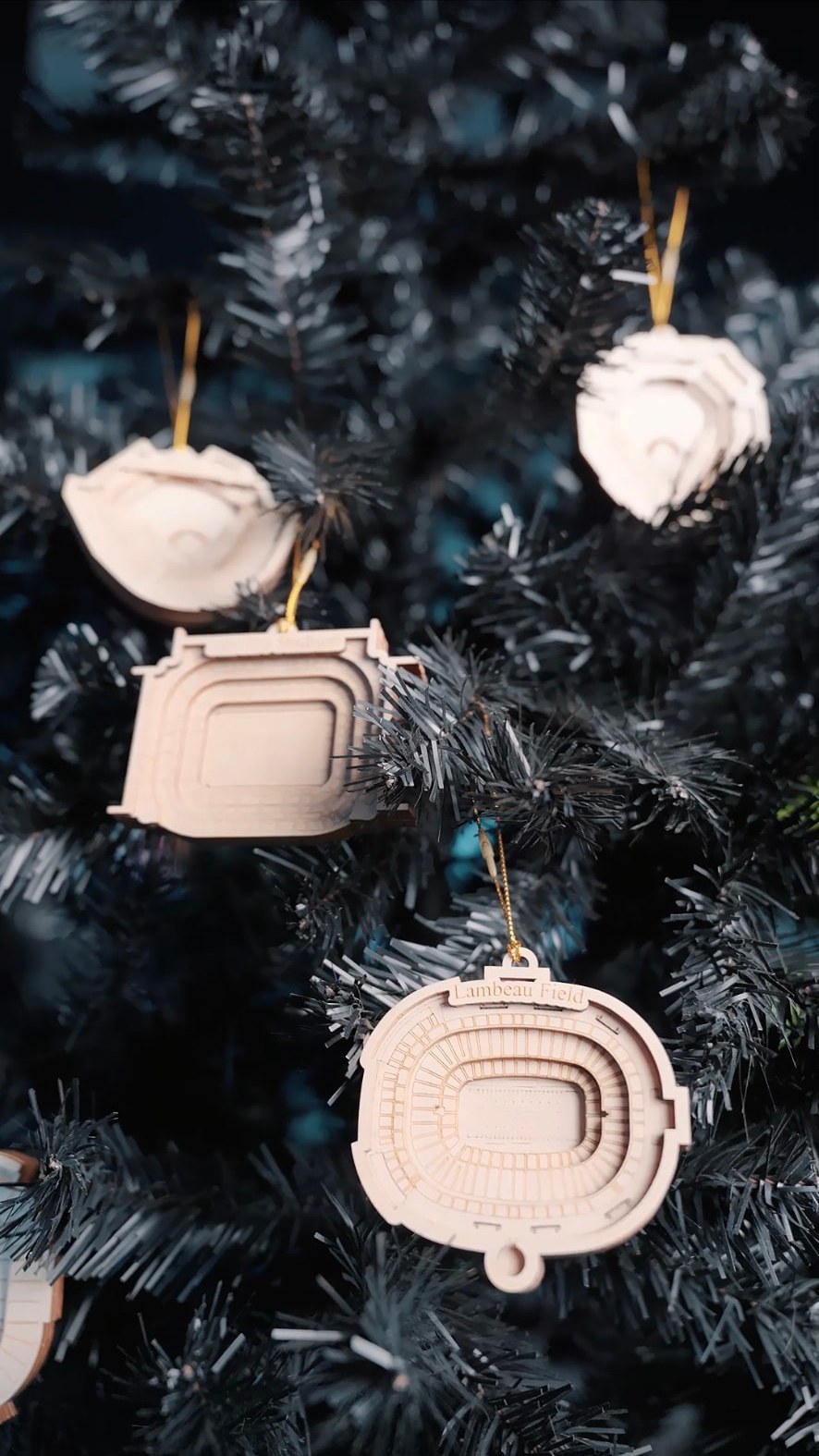 Layered 3D stadium ornaments, including Lambeau Field, hanging on a black Christmas tree